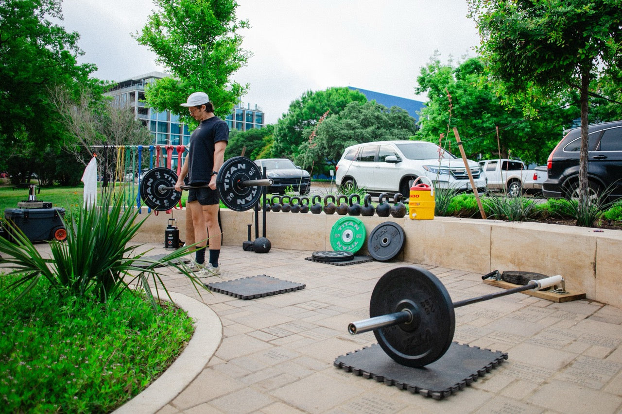 man deadlifting a rouge barbell with titan bumper plates at yudae wellness outdoor gym