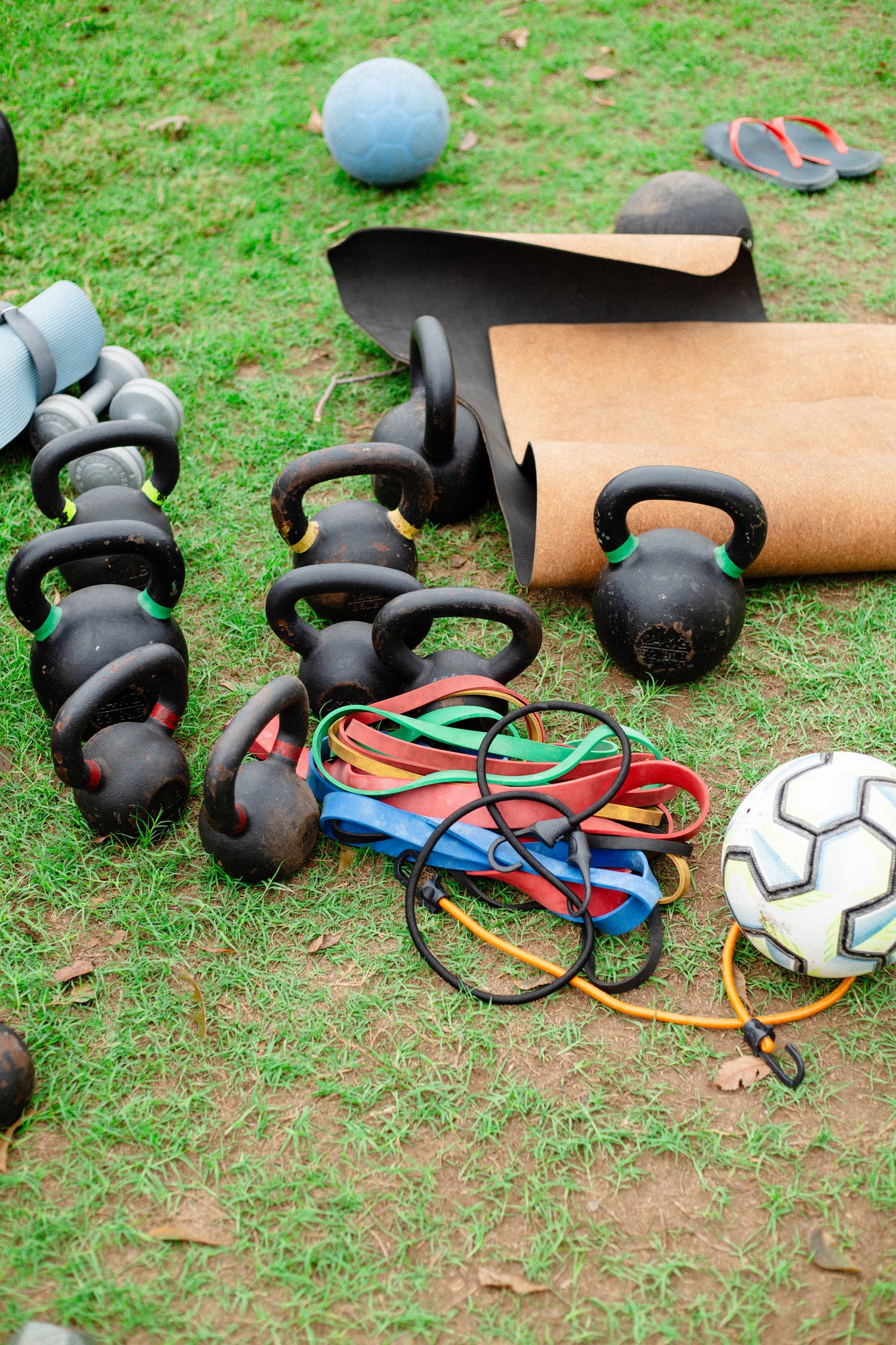 kettlebell weight variations splayed out on green lawn next to soccer balls, yoga mats, and power band resistance bands