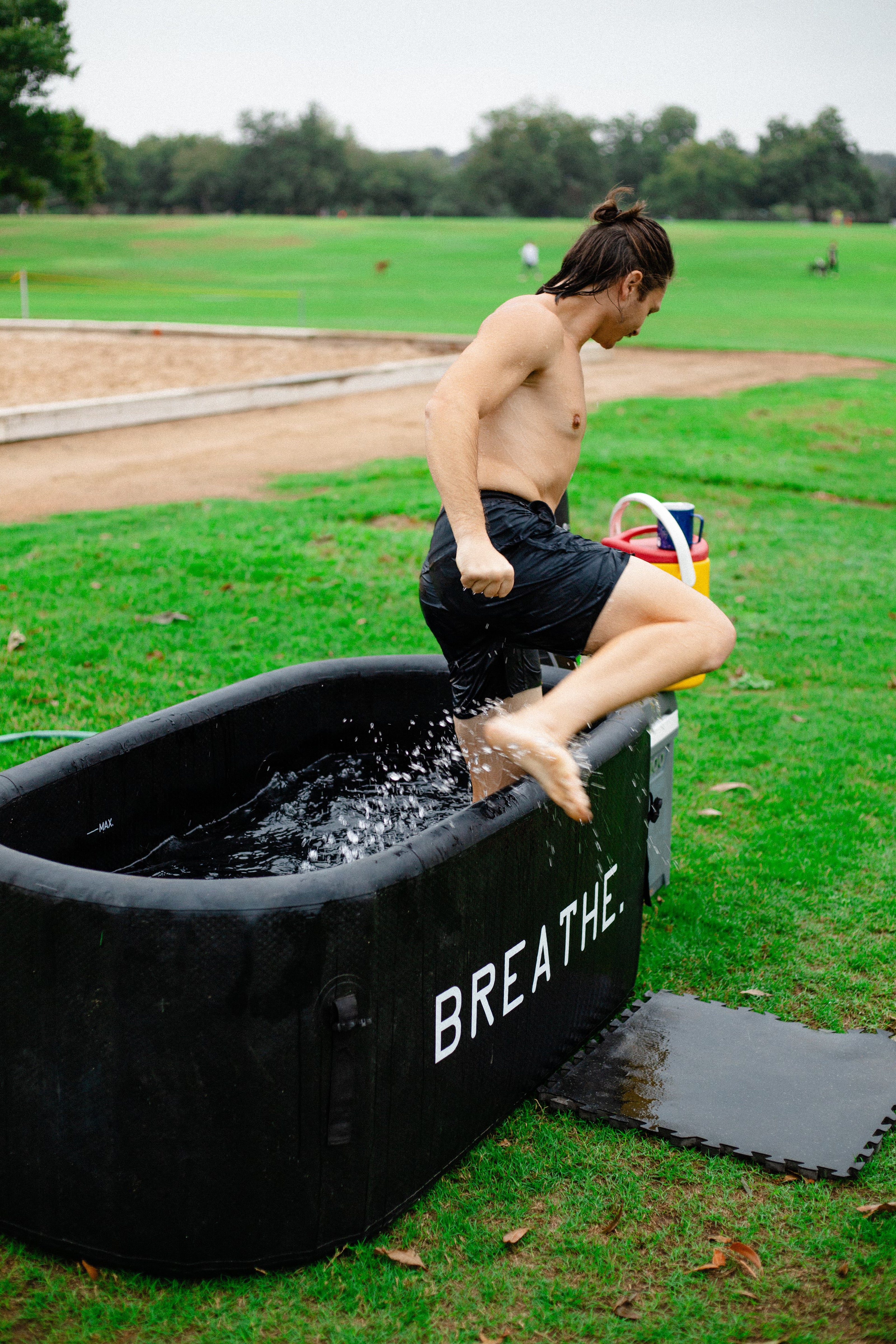 man stepping out of black ice bath with words "breathe" printed in white letters on a green lawn. 